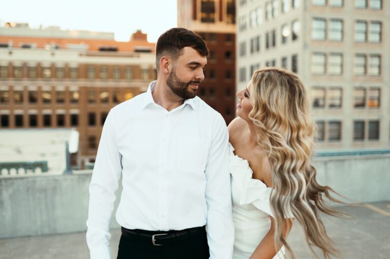bride looks at groom as she flips her hair and smiles on top of rooftop