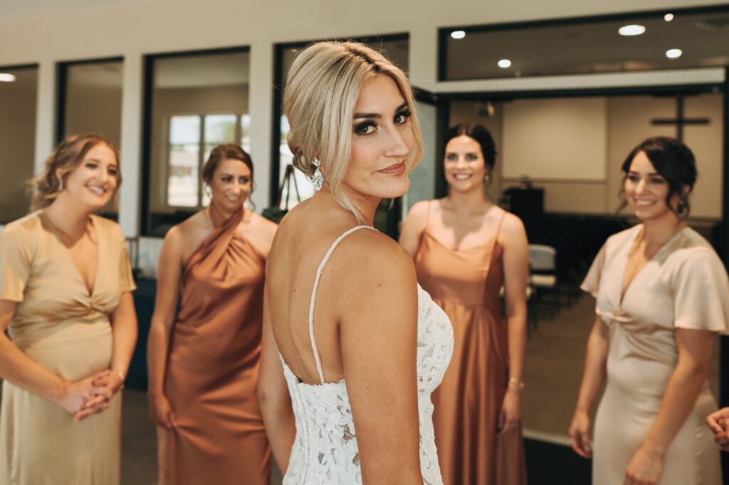 bride looks back at camera and smirks with bridesmaids in the background
