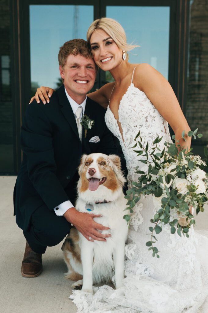 Bride and groom pose with dog for family portrait during wedding
