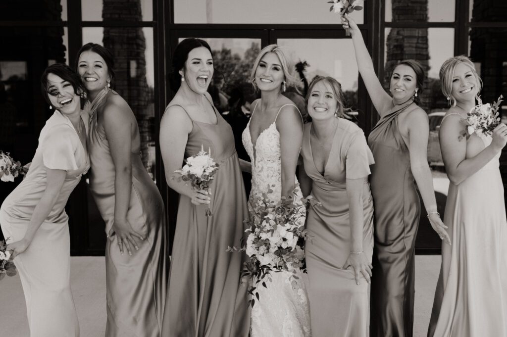 bridsmaids and bride pose silly in front of church black and white image