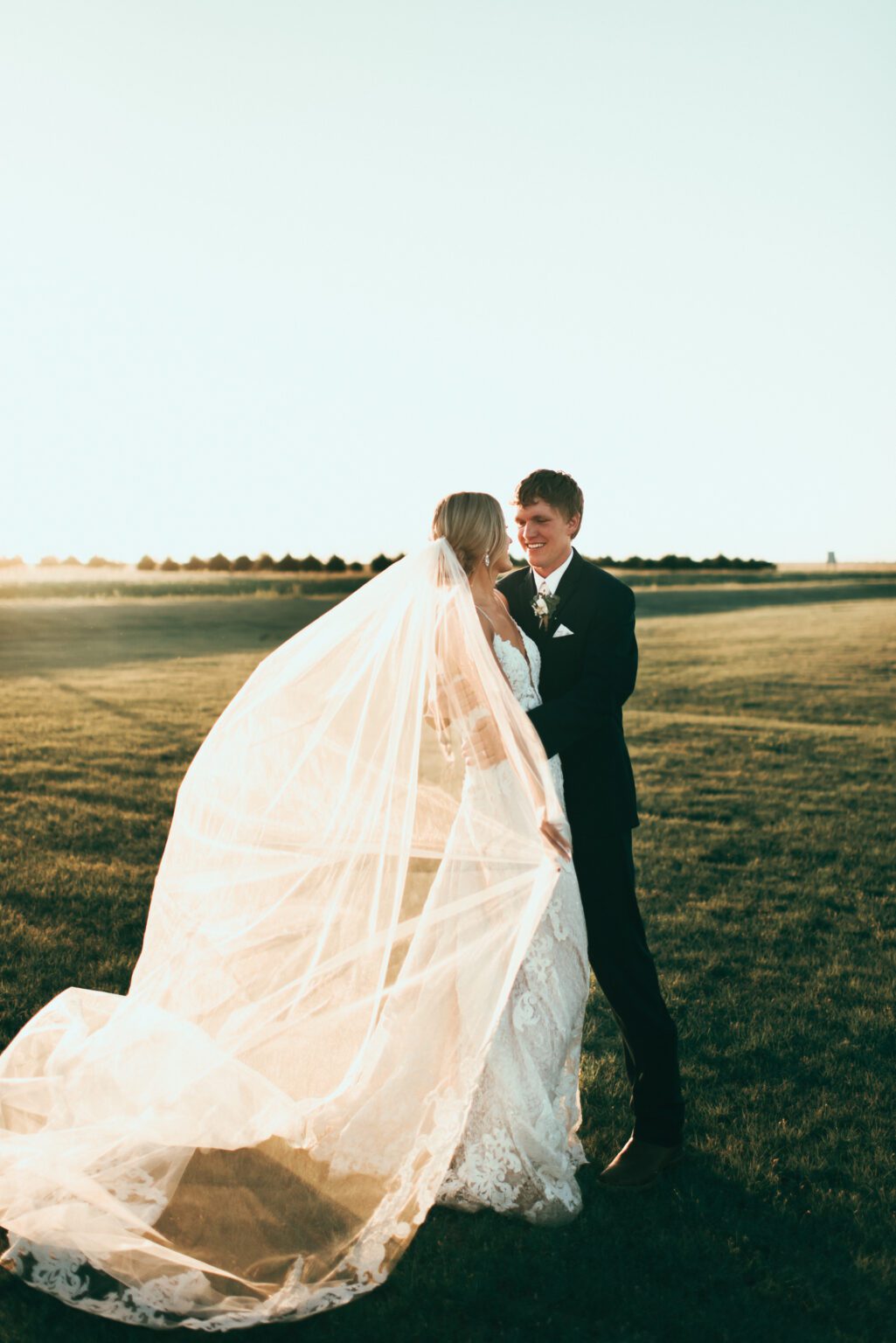 bride holds on to veil while wind catches it and groom hugs bride