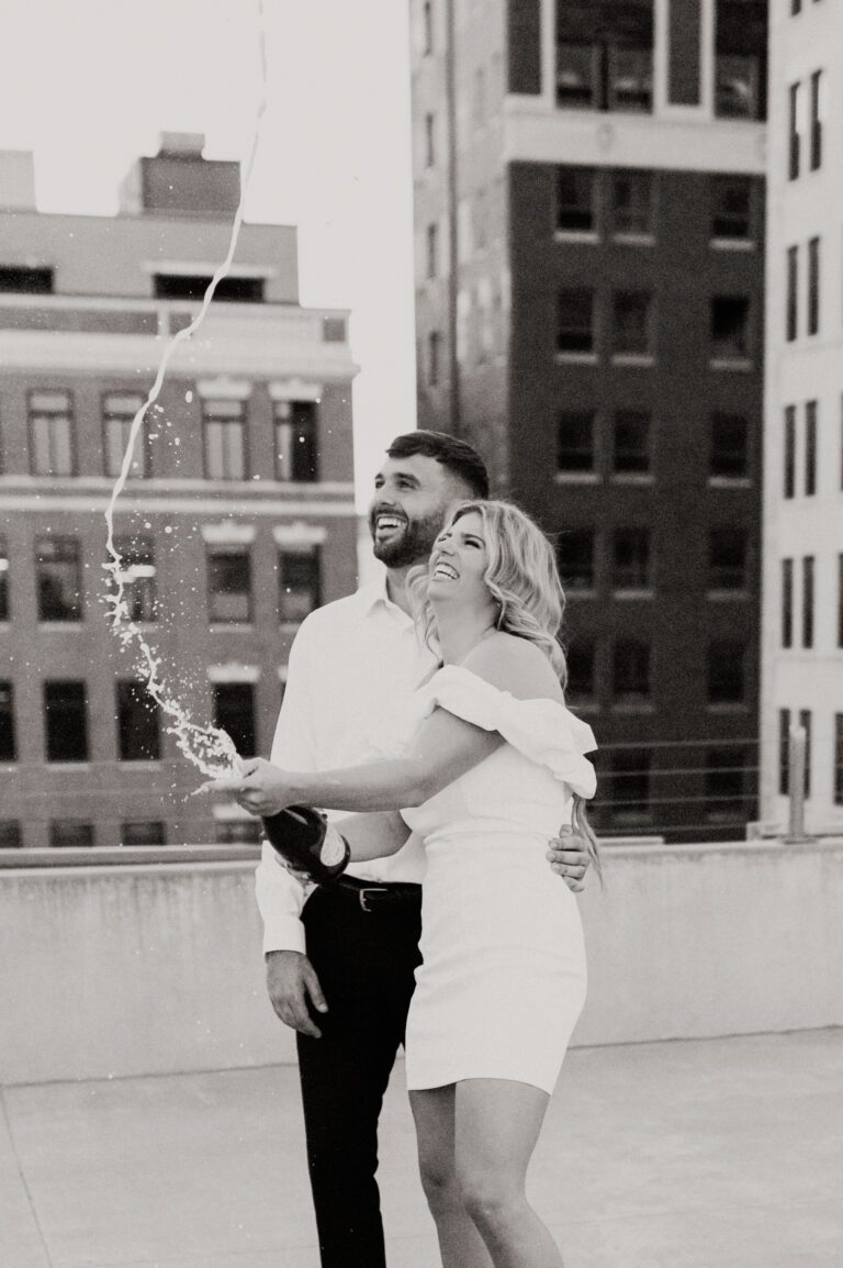 couple spraying champagne celebrating engagement on rooftop in downtown wichita kansas