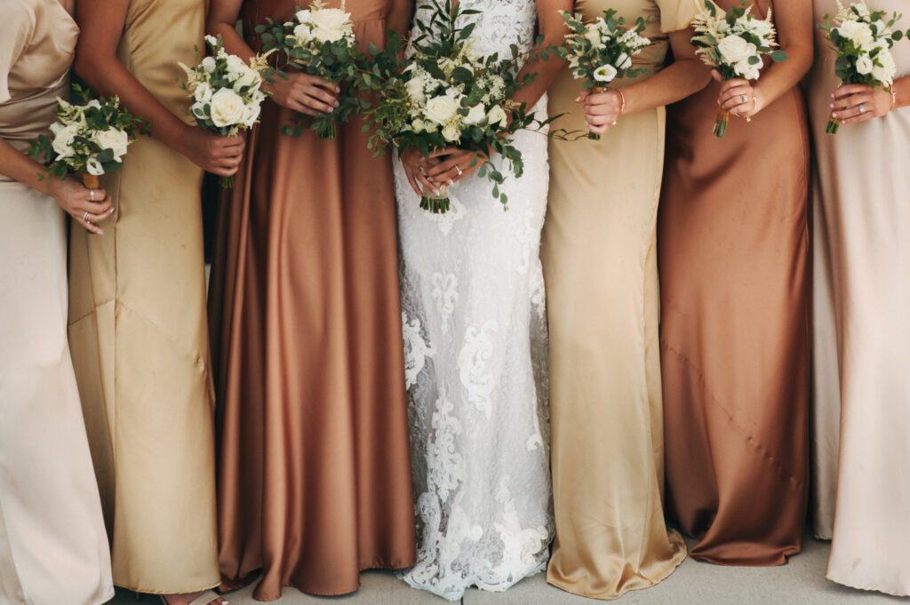 detail image of bridesmaids wearing brown and gold silk bridesmaid dresses and holding green and white timeless bouquet of flowers