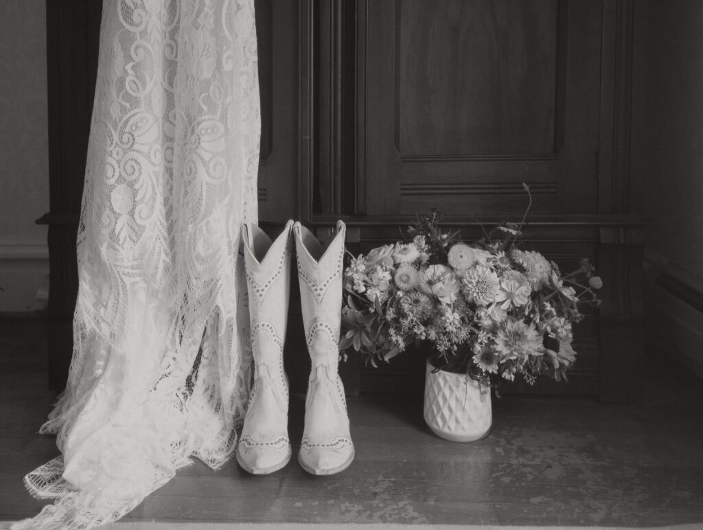 black and white wedding photo of lace wedding dress, cowgirl boots and wedding bouquet at Clover Cliff Ranch