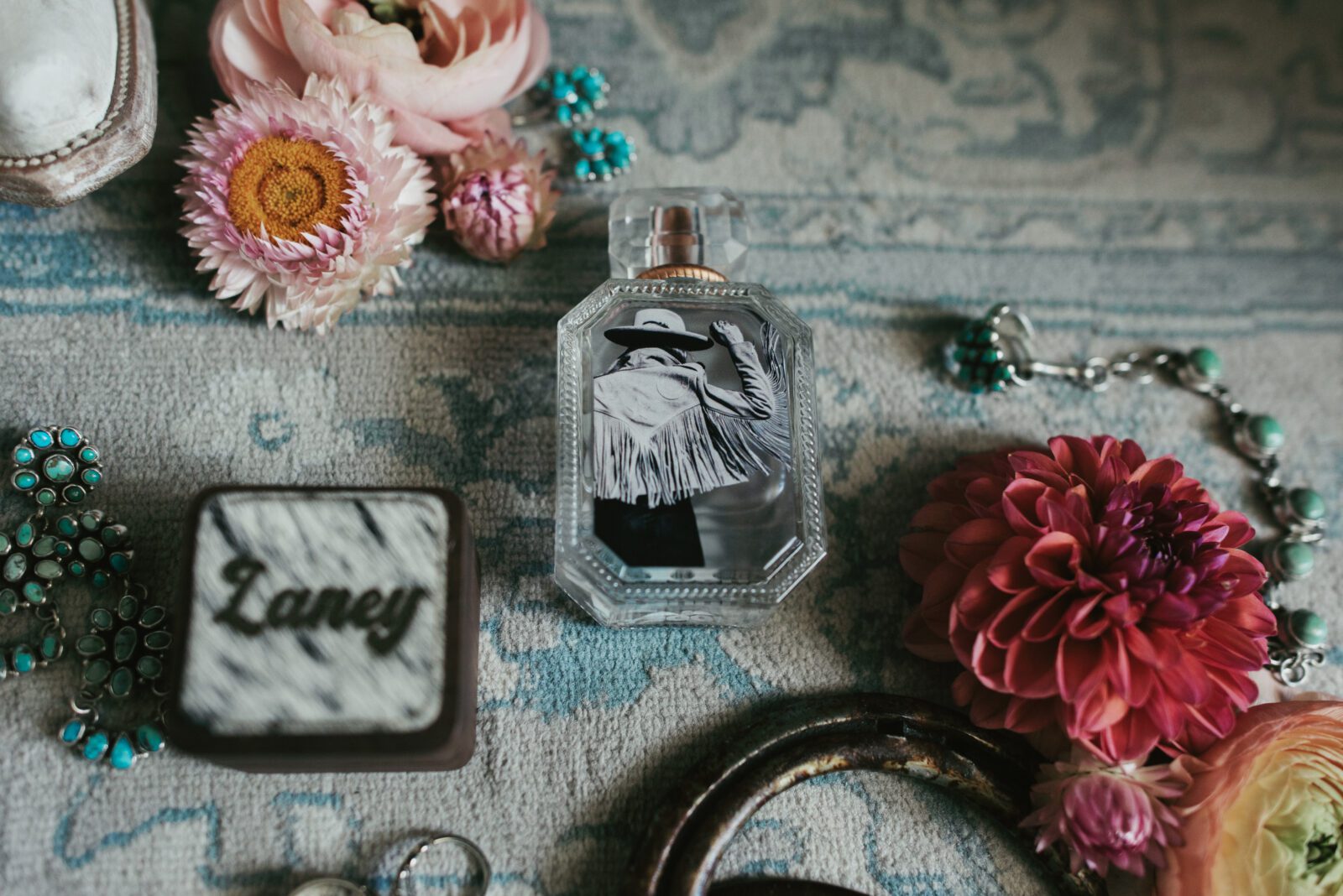 wedding details, perfume, ring box and wedding florals scattered on rug