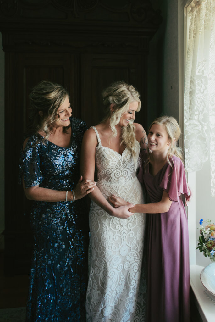 mother, bride and sister hold each other and laugh before wedding ceremony starts