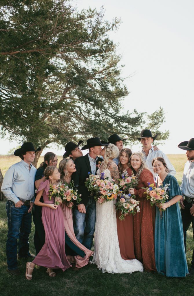 wedding photo of wedding party gathering around bride and groom in mismatched colored dresses and wildflower florals at clover cliff ranch
